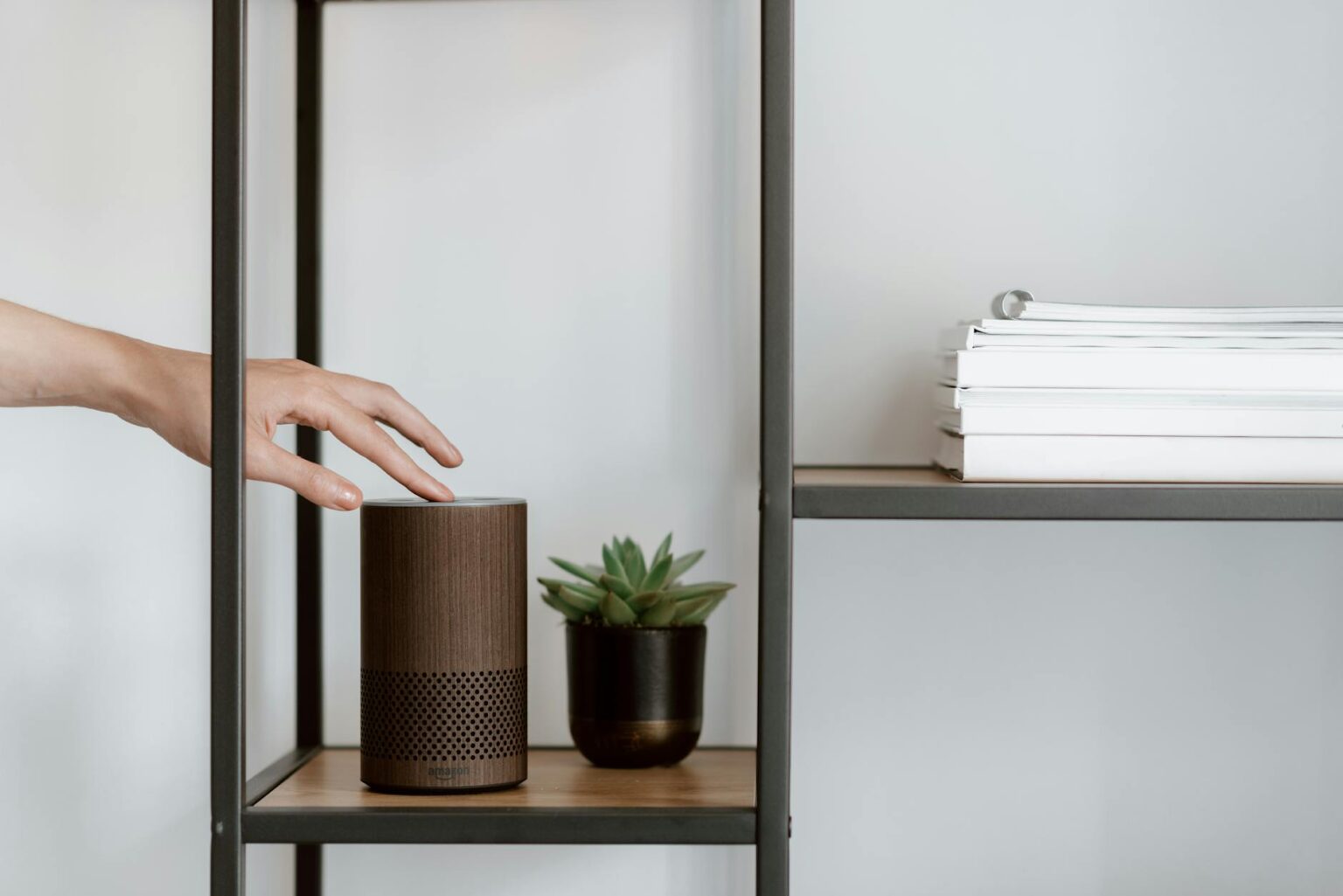 A pair of compact wireless bookshelf speakers on a wooden shelf in a modern living room