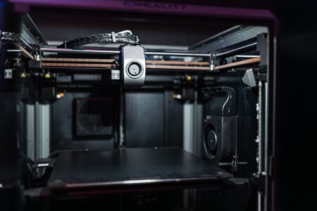 A compact desktop 3D printer producing a small object on its print bed