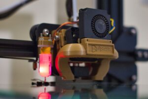 A modern desktop 3D printer producing a detailed plastic model on a build plate