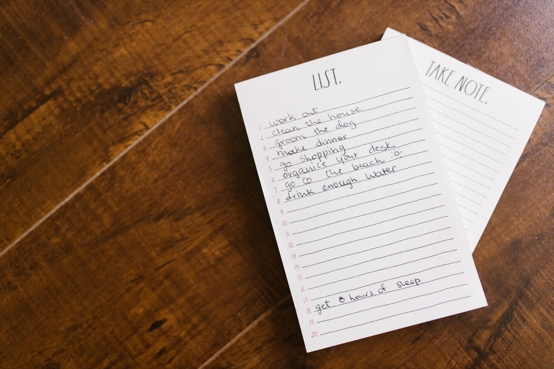 A handwritten grocery shopping list on a notepad next to fresh vegetables